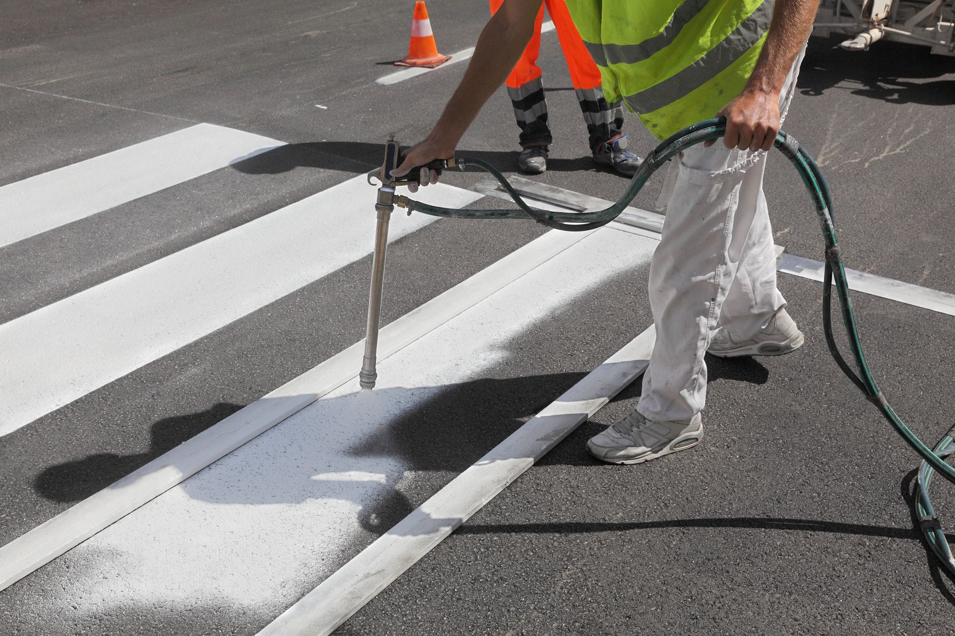 Worker spraying pedestrian crosswalk at a street, repairing and painting.