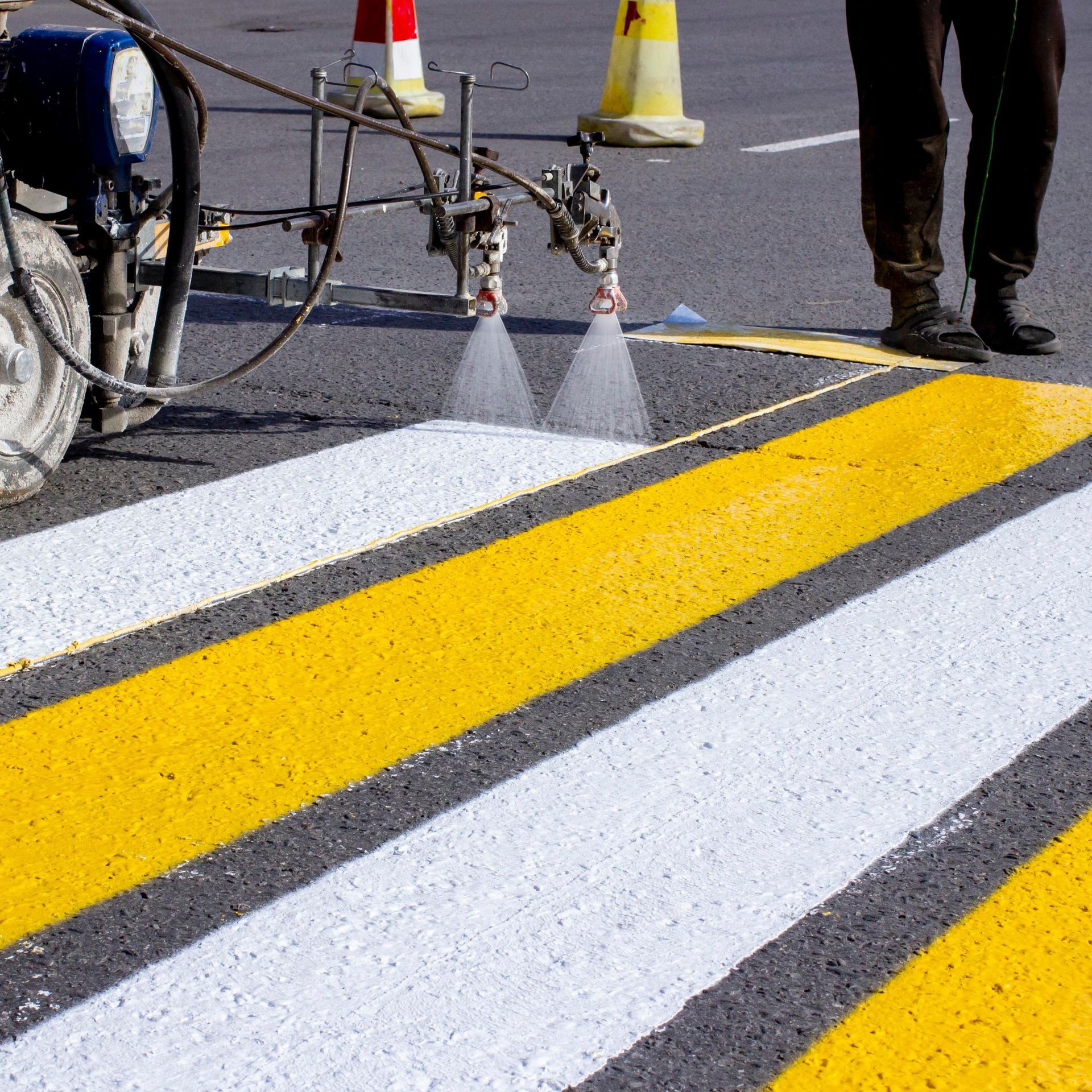 Worker applying fresh white crosswalk lines on an asphalt road surface.