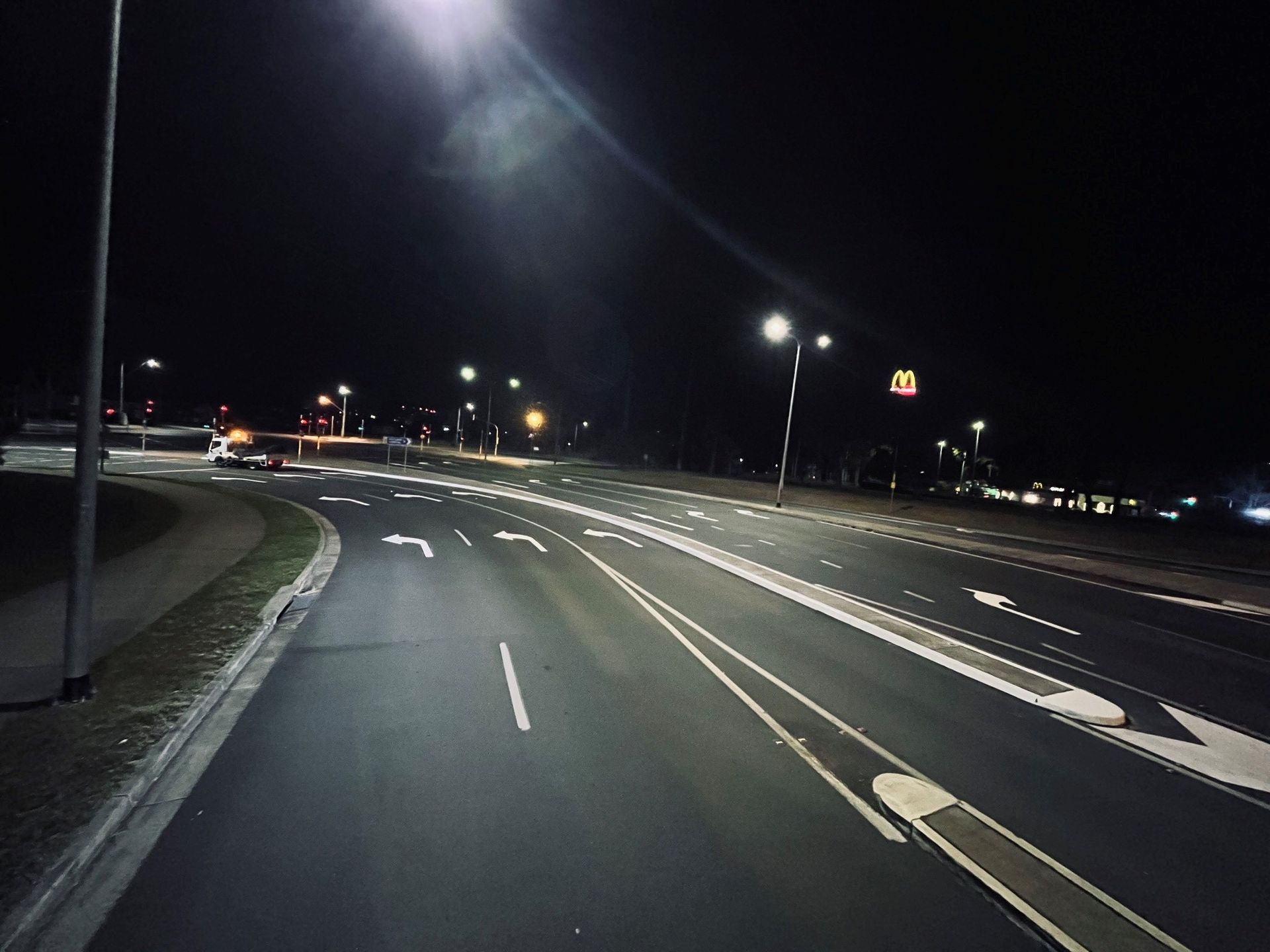 An empty highway at night with a mcdonald 's in the background