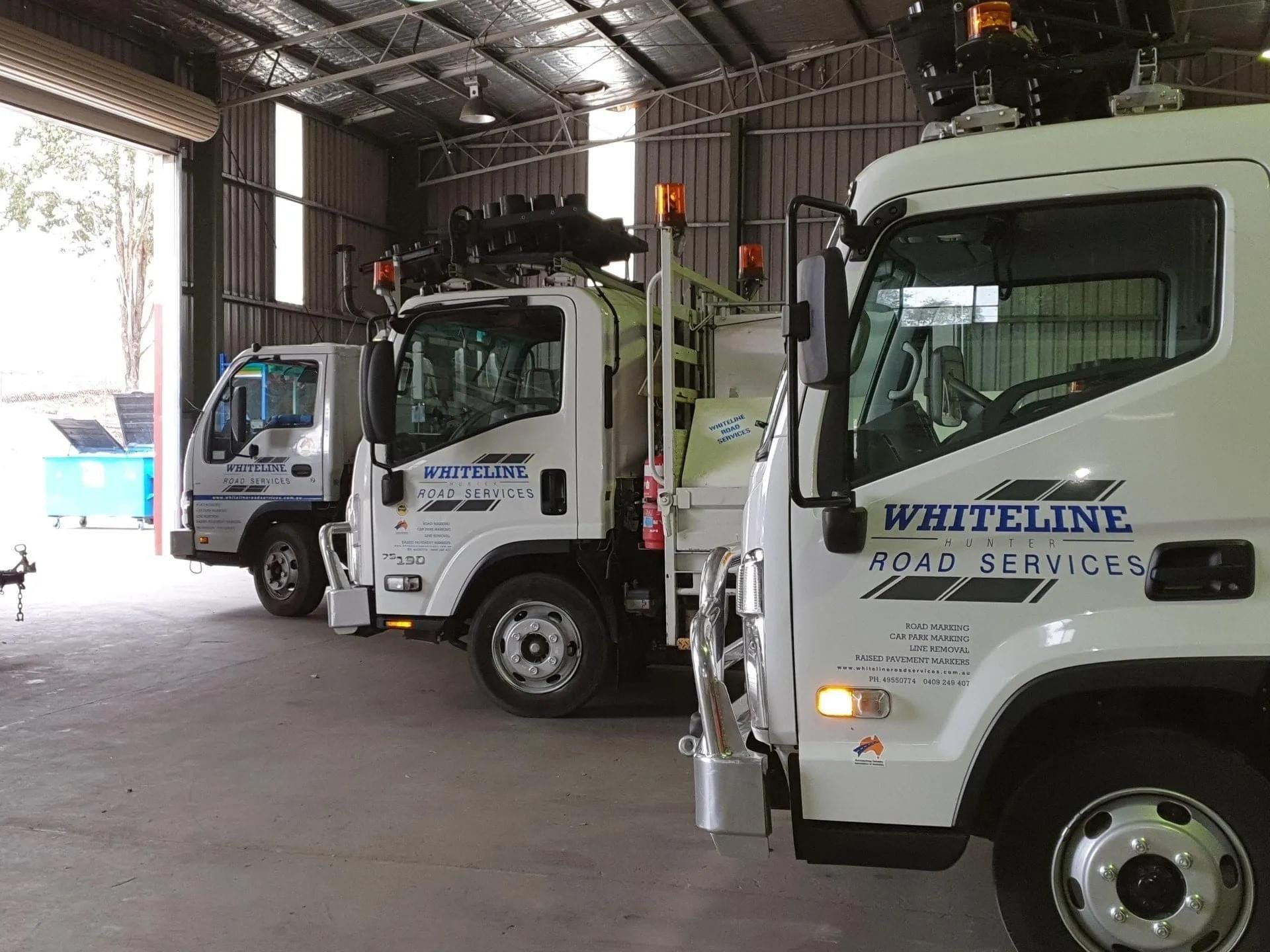 Three white utility trucks parked inside a warehouse, one labeled Whiteline Civil Service.