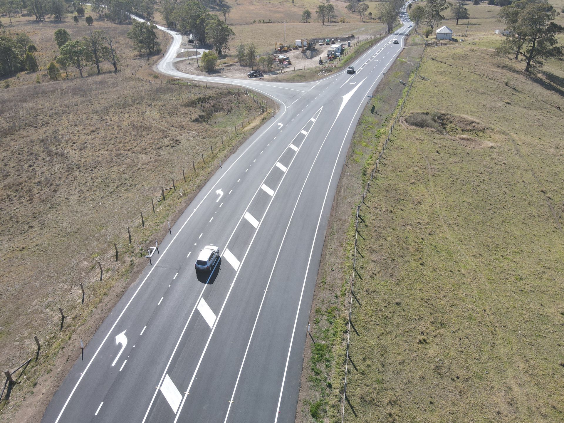 An aerial view of a highway with a white car driving down it