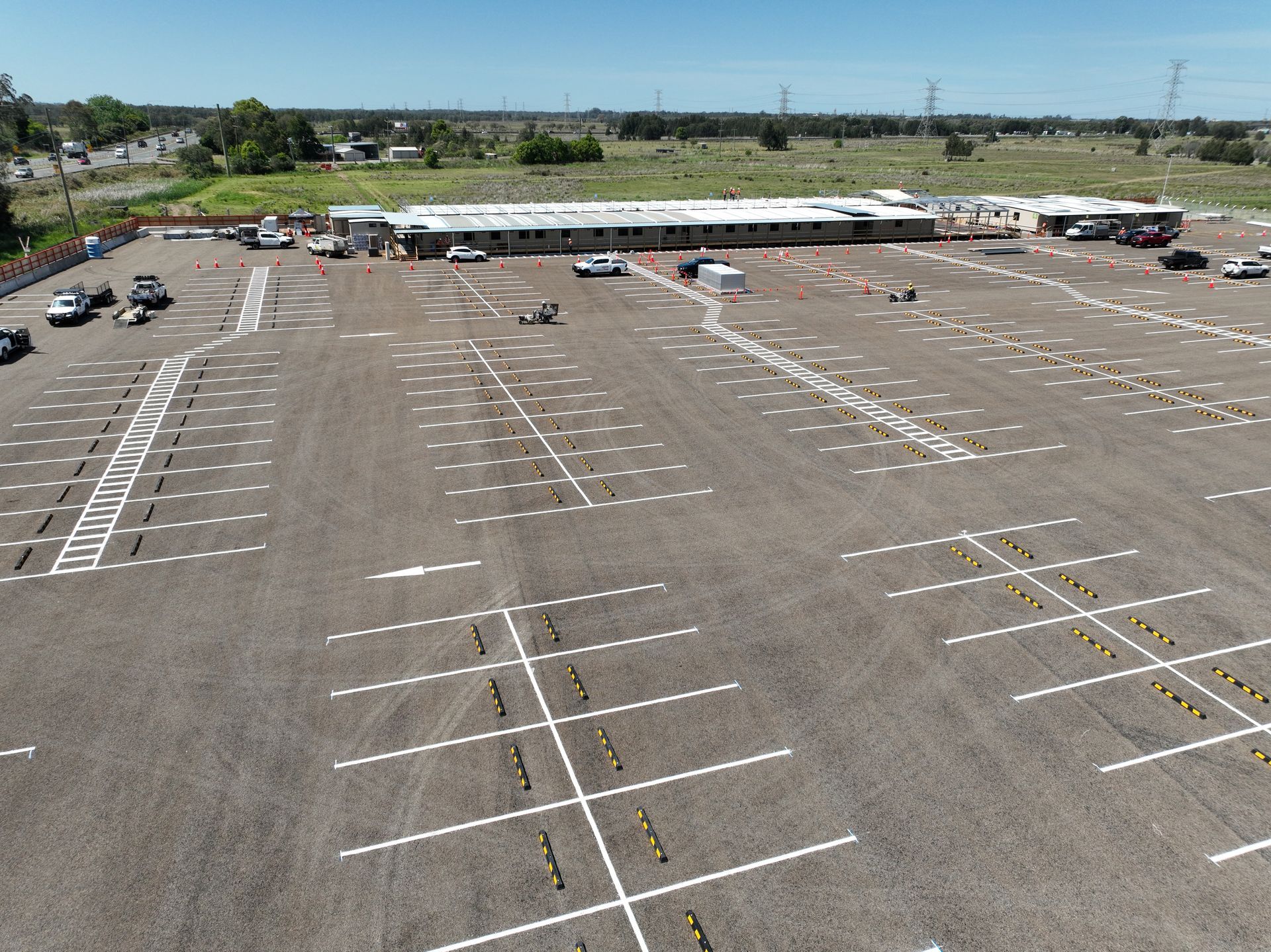 Empty outdoor parking lot with painted white lines and a few cars along the far edge.