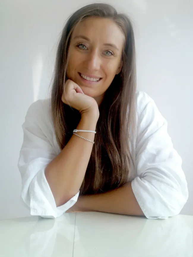 A woman in a white shirt is smiling with her hand on her chin