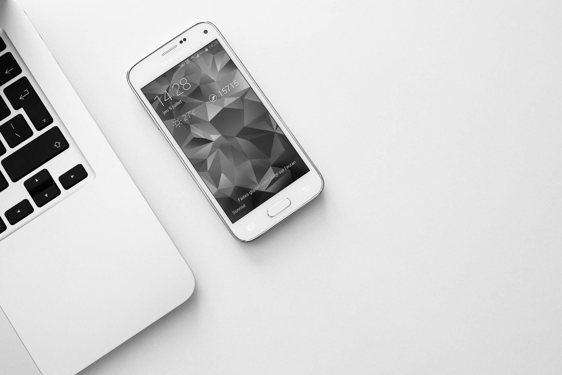 A cell phone is sitting next to a laptop on a table.