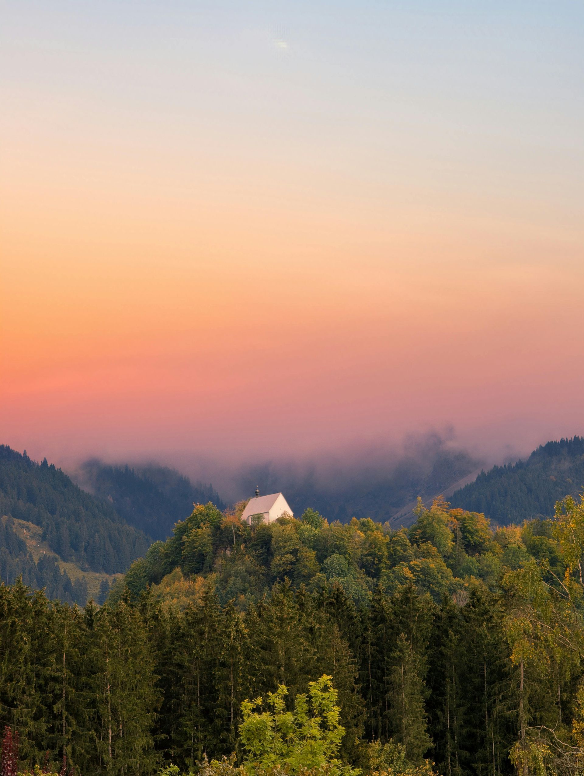 A house is sitting on top of a hill in the mountains at sunset.