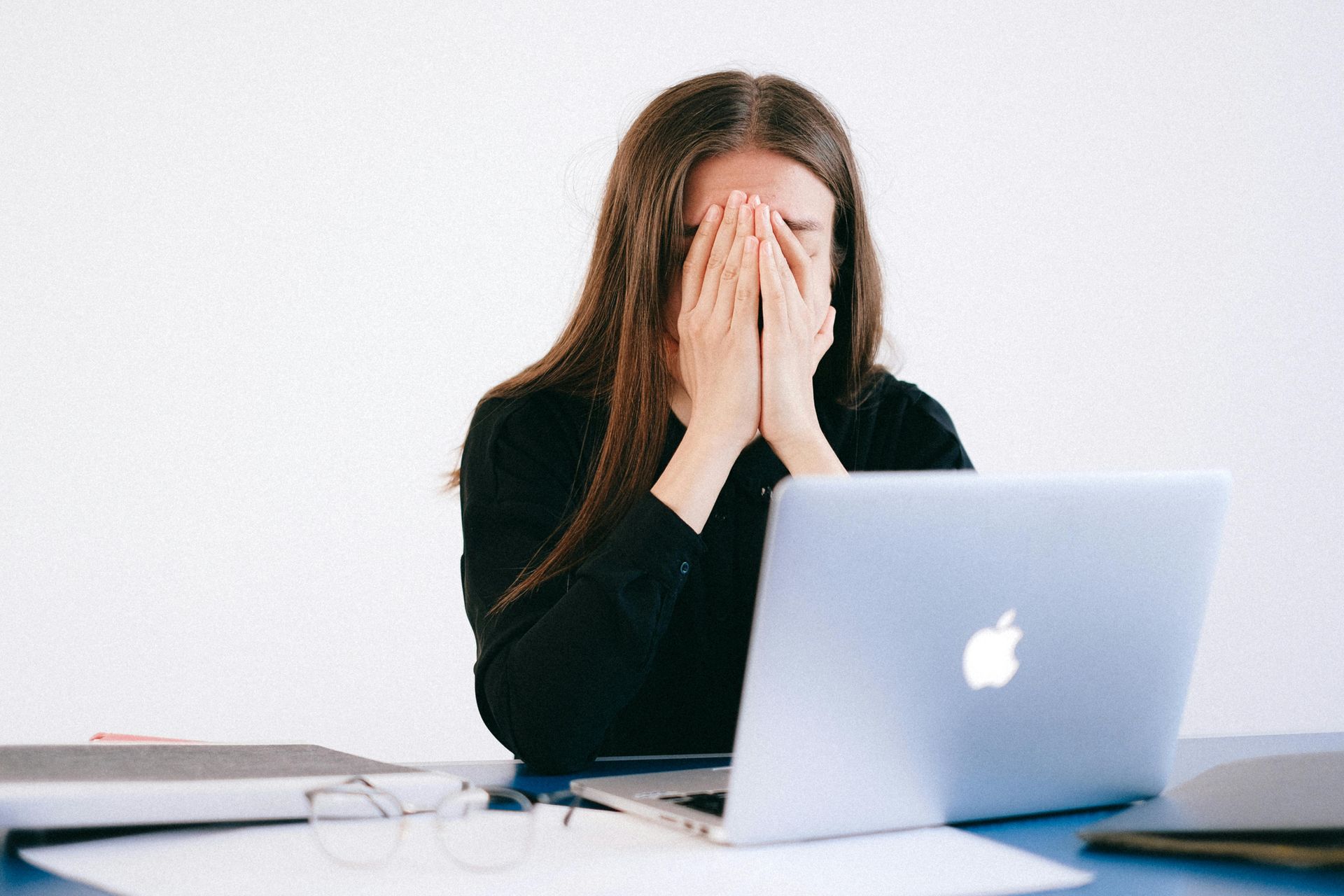 A woman is covering her face while using a laptop computer.