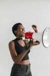 A person wearing a black top yells into a red and white megaphone with one fist raised against a light gray background.