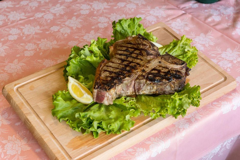 Fettine di bistecca al sangue su un piatto nero con erbe aromatiche, pomodorini e uno spicchio d'aglio
