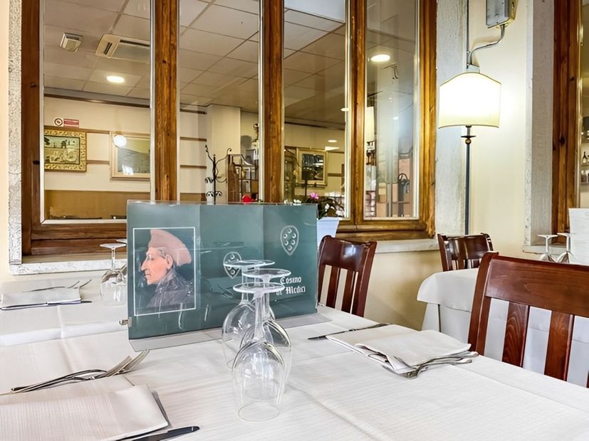 Tavolo da ristorante apparecchiato con tovaglie bianche, bicchieri e menù esposto davanti a grandi specchi a parete.