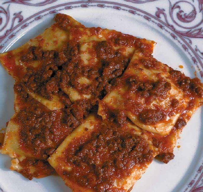 Piatto di ravioli conditi con salsa di pomodoro rosso su un piatto decorato.