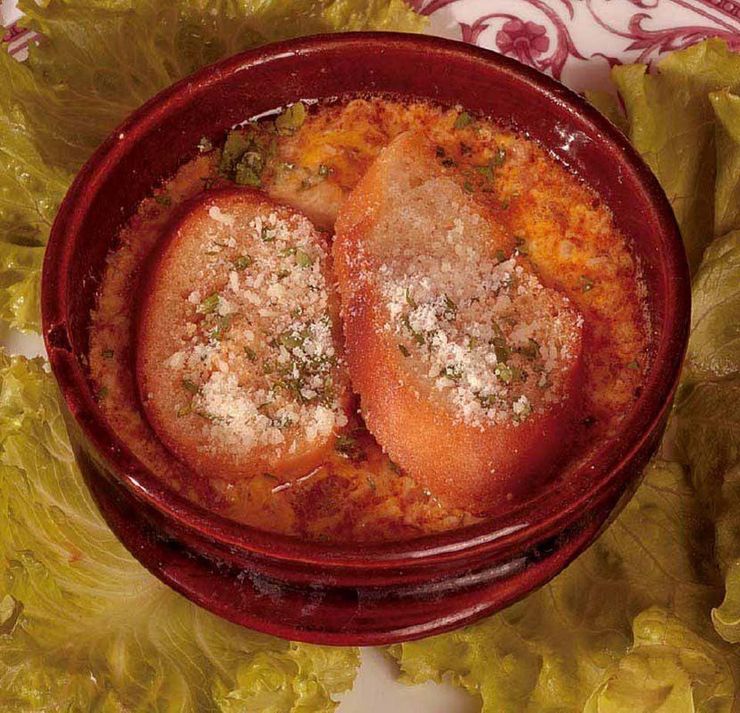 Zuppa in una ciotola rossa, guarnita con crostini e formaggio grattugiato su foglie di lattuga.
