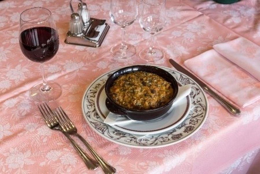 Una tavola apparecchiata con vino rosso, posate e un piatto al forno su una tovaglia rosa.