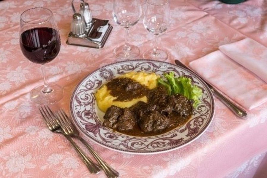 Primo piano di una bistecca grigliata con il centro rosato su un letto di verdure, su uno sfondo scuro.