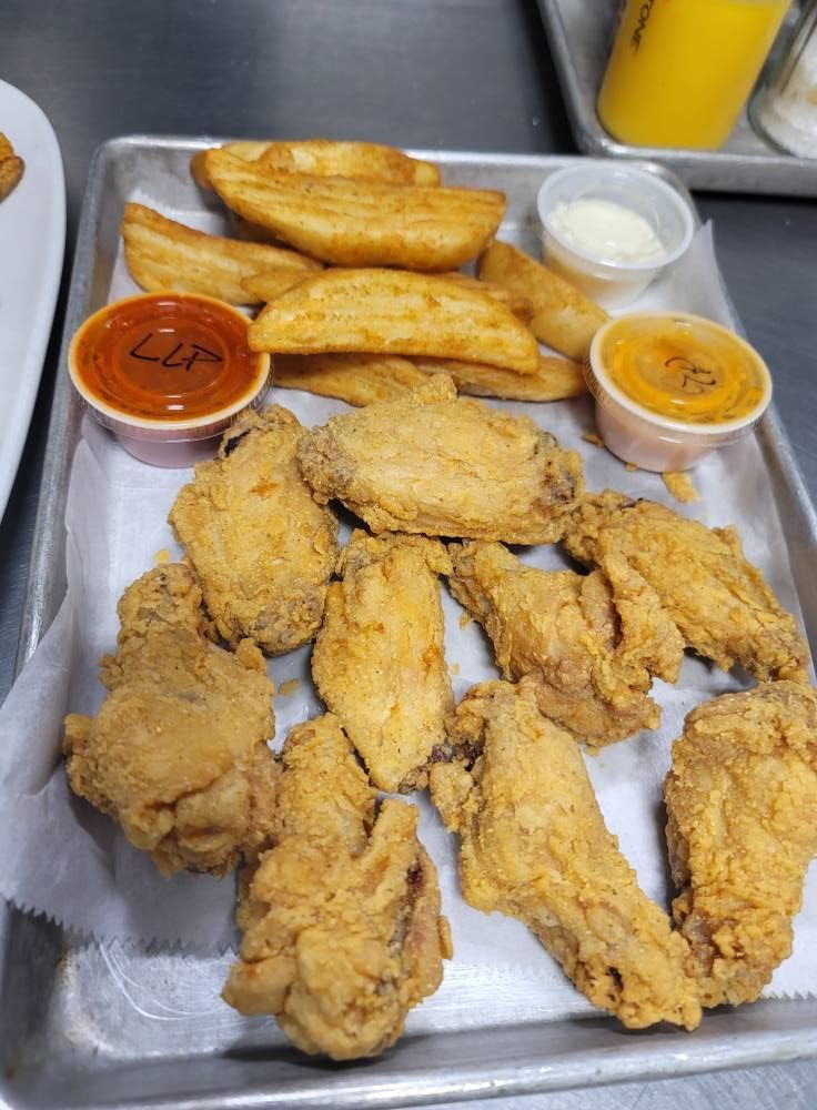Fried chicken wings, potato wedges, and dipping sauces on a tray.