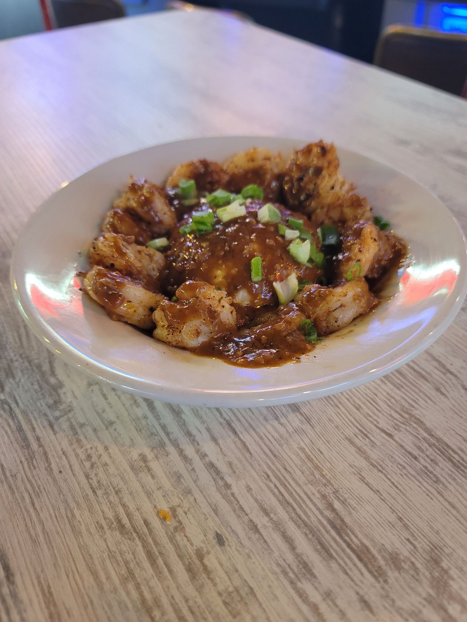 Fried shrimp over grits, topped with gravy and green onions, served on a white plate on a wood table.