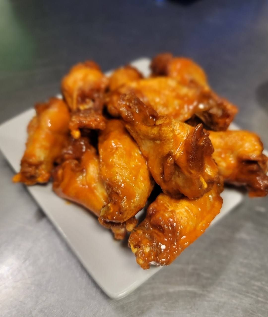 A pile of golden-brown chicken wings with glossy sauce on a square white plate.