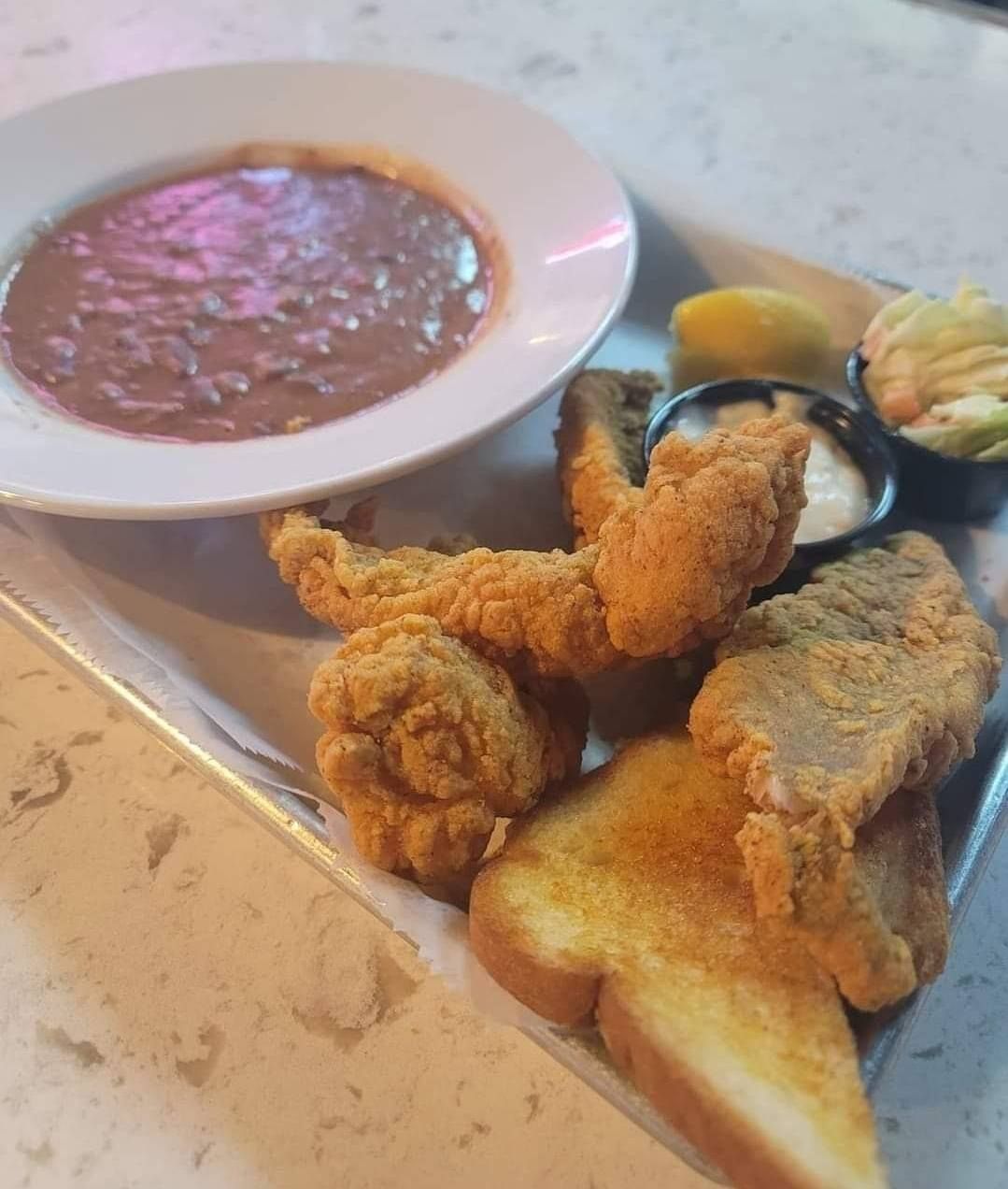 Fried catfish with red beans, toast, coleslaw, lemon wedge, and sauce on a tray.