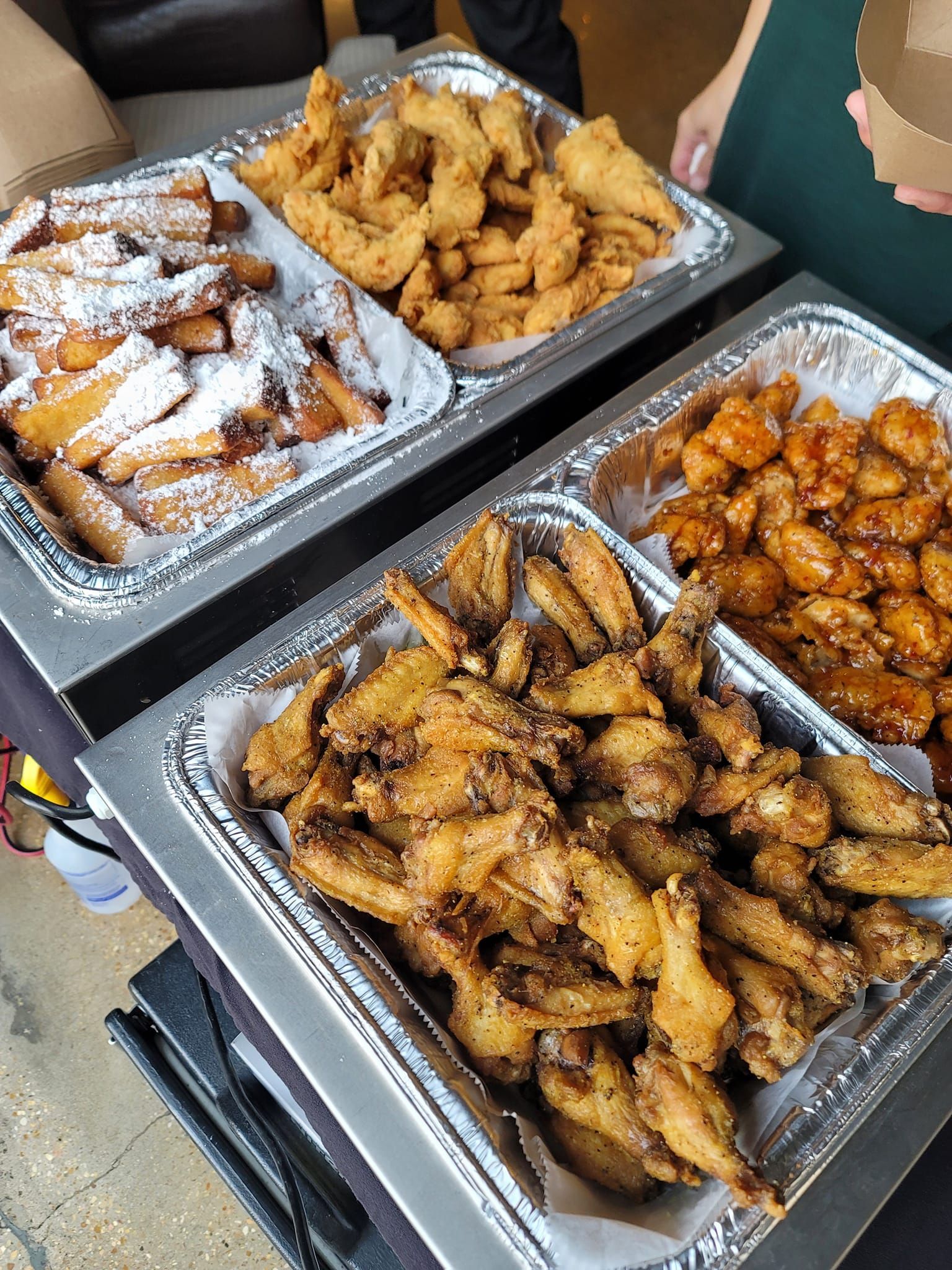 Buffet trays with fried chicken, wings, and french toast sticks covered in powdered sugar.