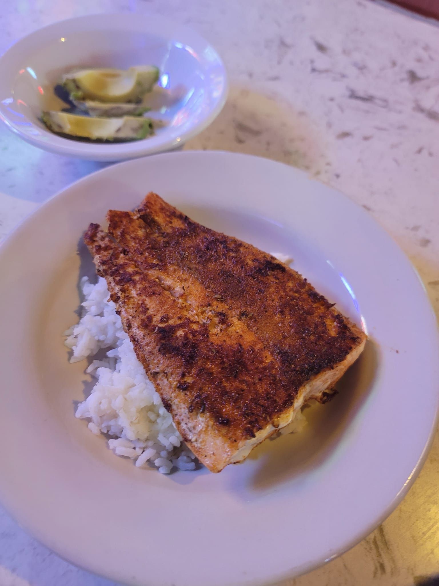 Plate of seasoned salmon on white rice, pickles on the side.