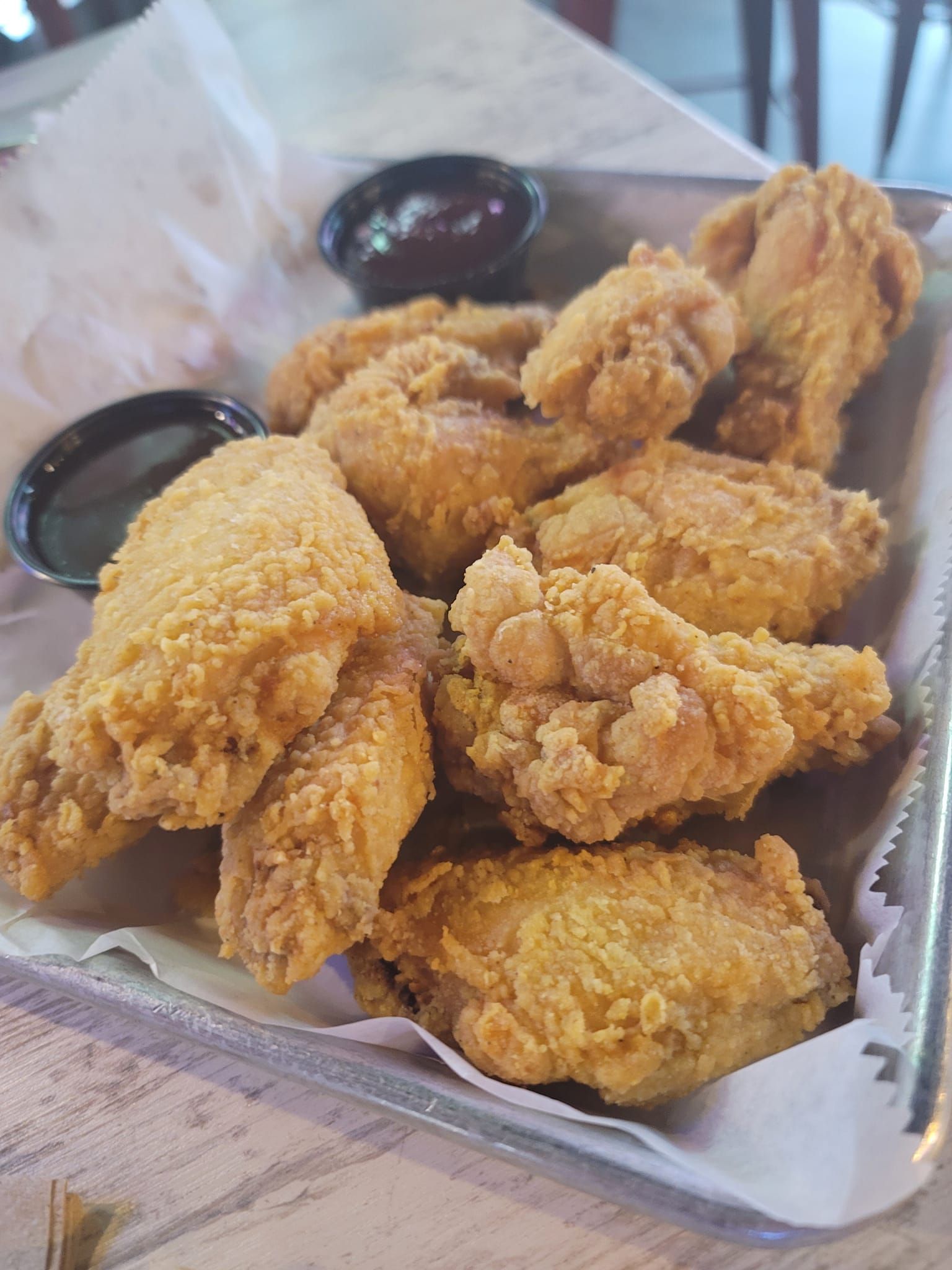 Fried chicken wings on a tray with two small bowls of dark sauce.