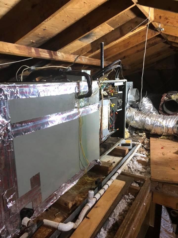 An attic with a lot of pipes and wires hanging from the ceiling.