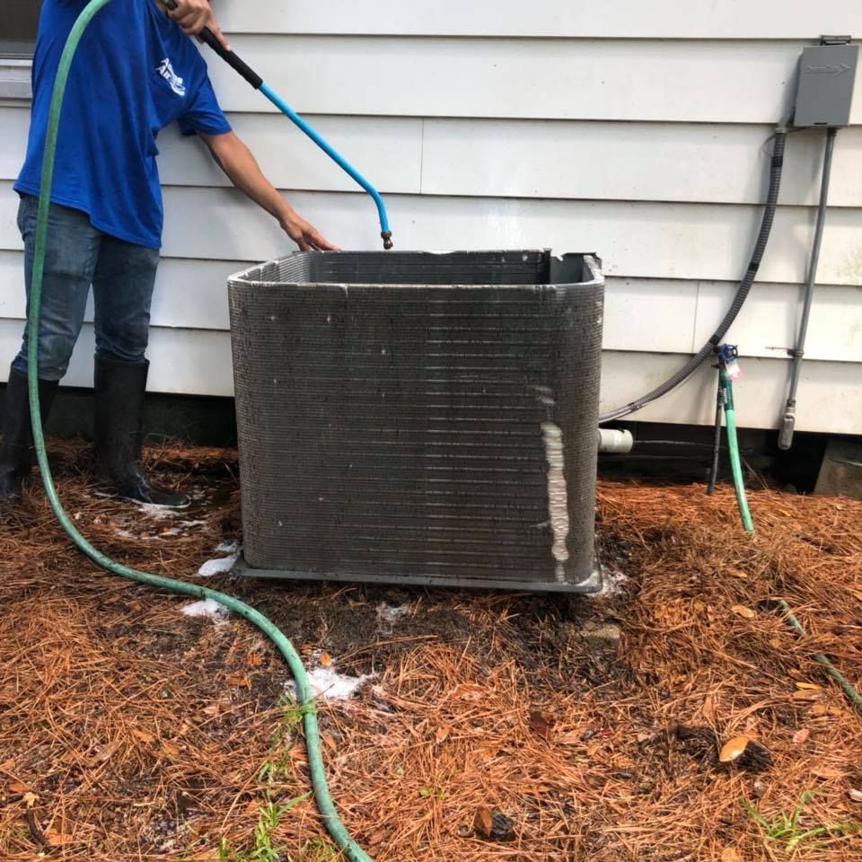 A man in a blue shirt is cleaning an air conditioner with a hose