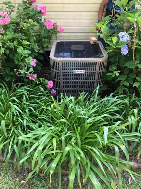 An air conditioner is sitting in the middle of a garden surrounded by flowers.