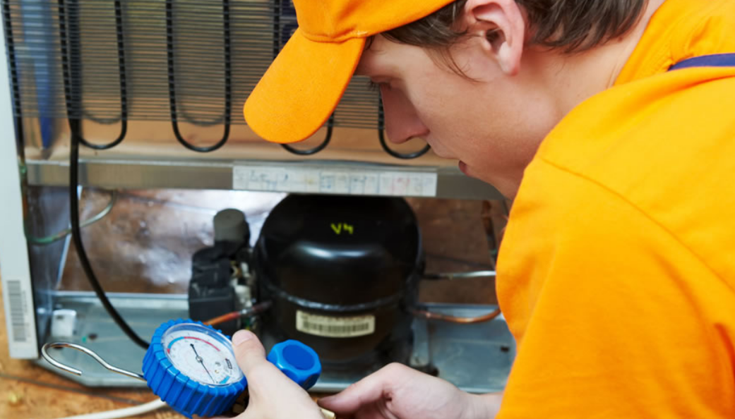 A man in an orange shirt is working on a refrigerator.