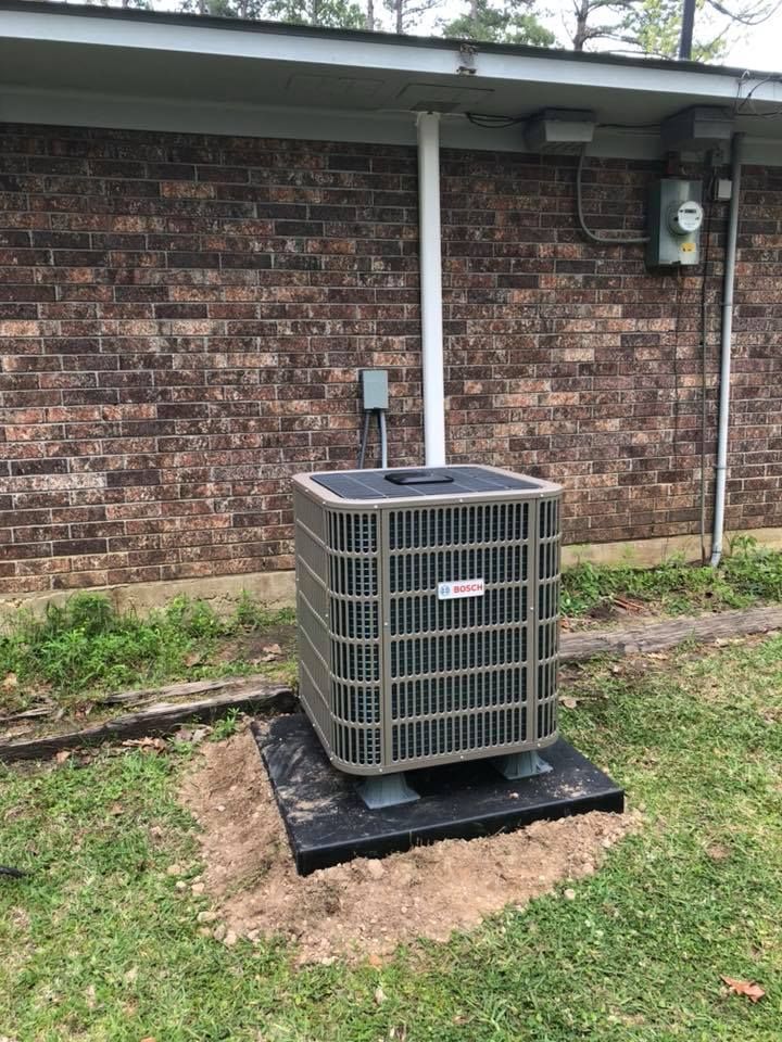A large air conditioner is sitting in the grass in front of a brick building.