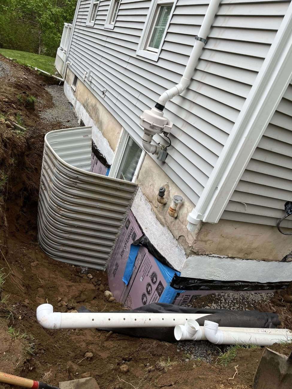 Completed French drain pipe installation with drainage stone along house foundation