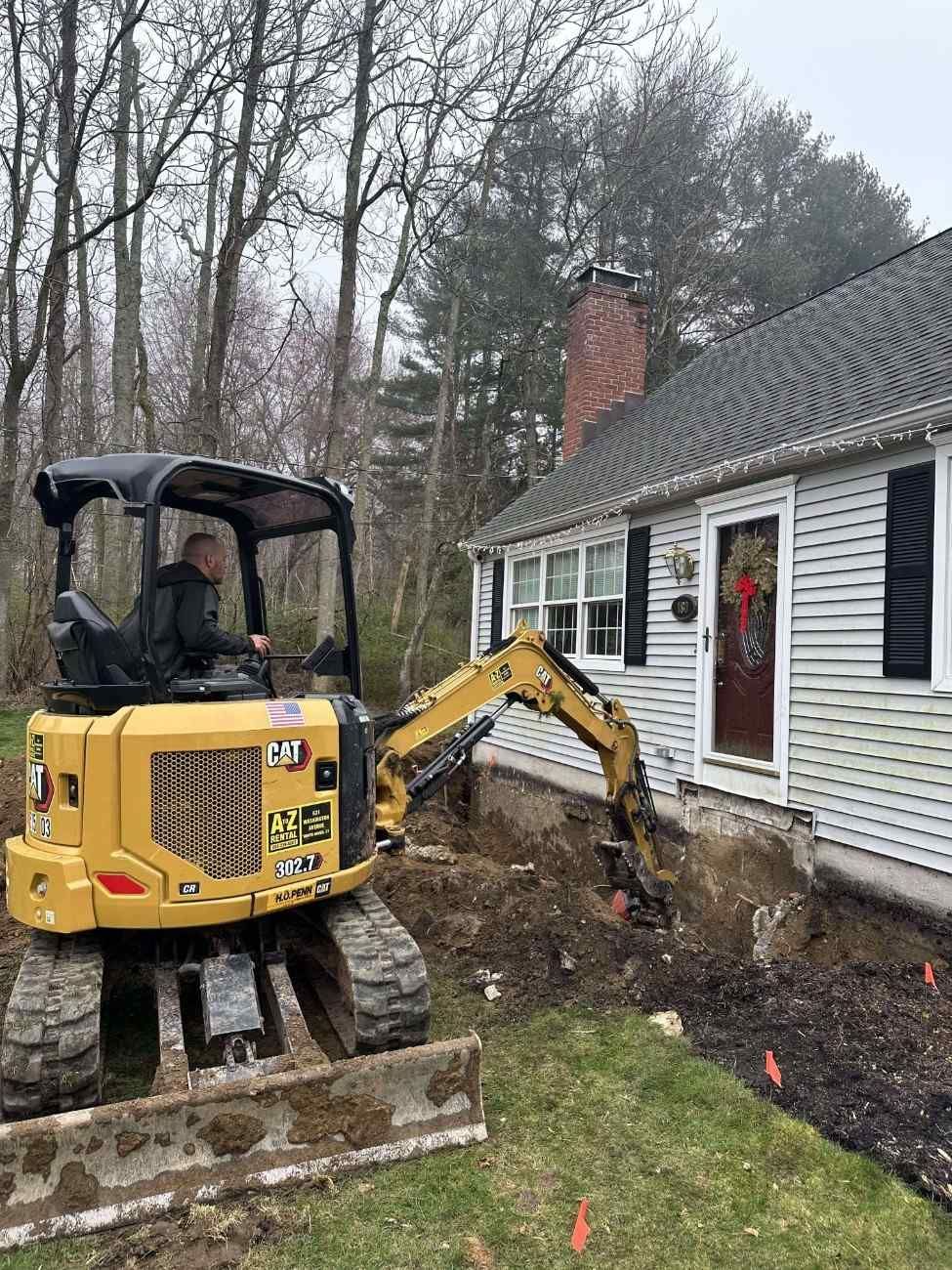 Excavator digging drainage trench next to residential foundation