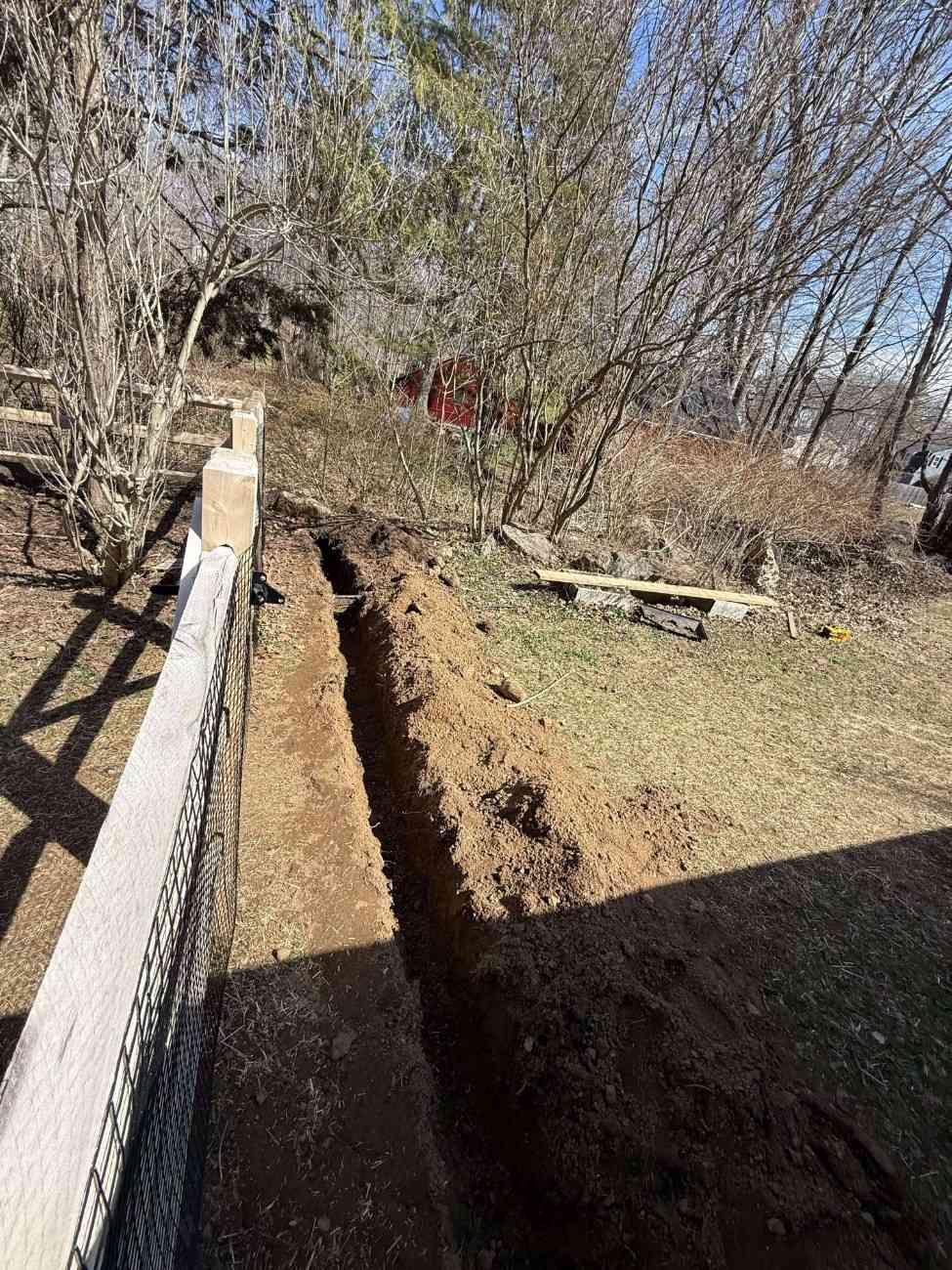 French drain trench installation along property fence line showing proper depth and grade