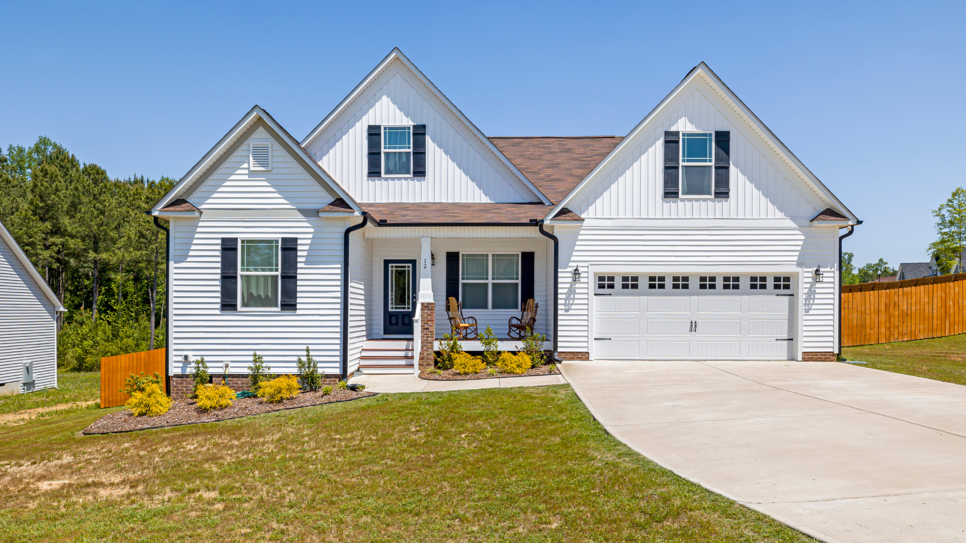 White suburban house with a two-car garage, front porch, and driveway under a clear sky