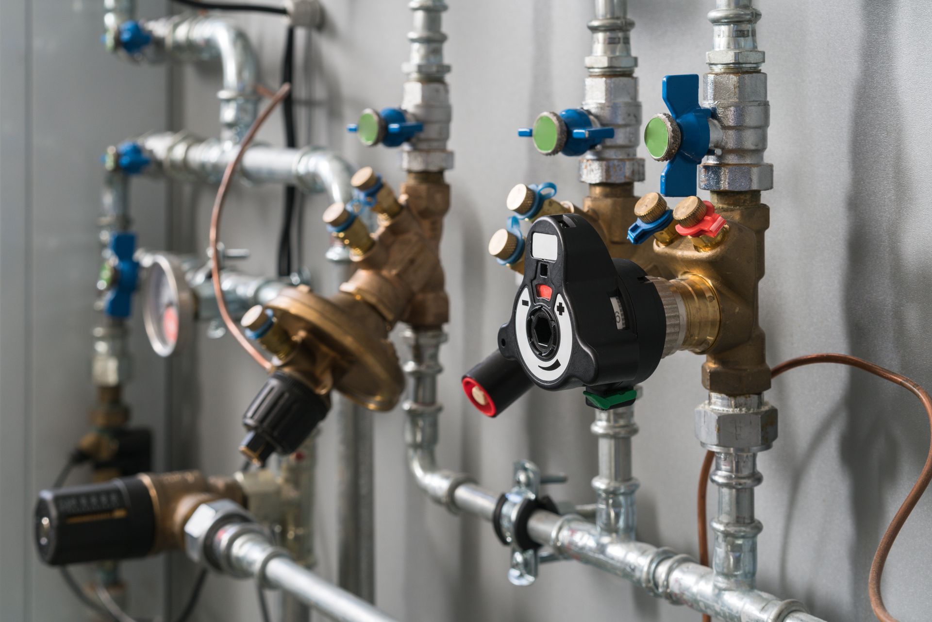 Pipes and valves on a wall. Brass and silver pipes with blue, red, and green valve handles.