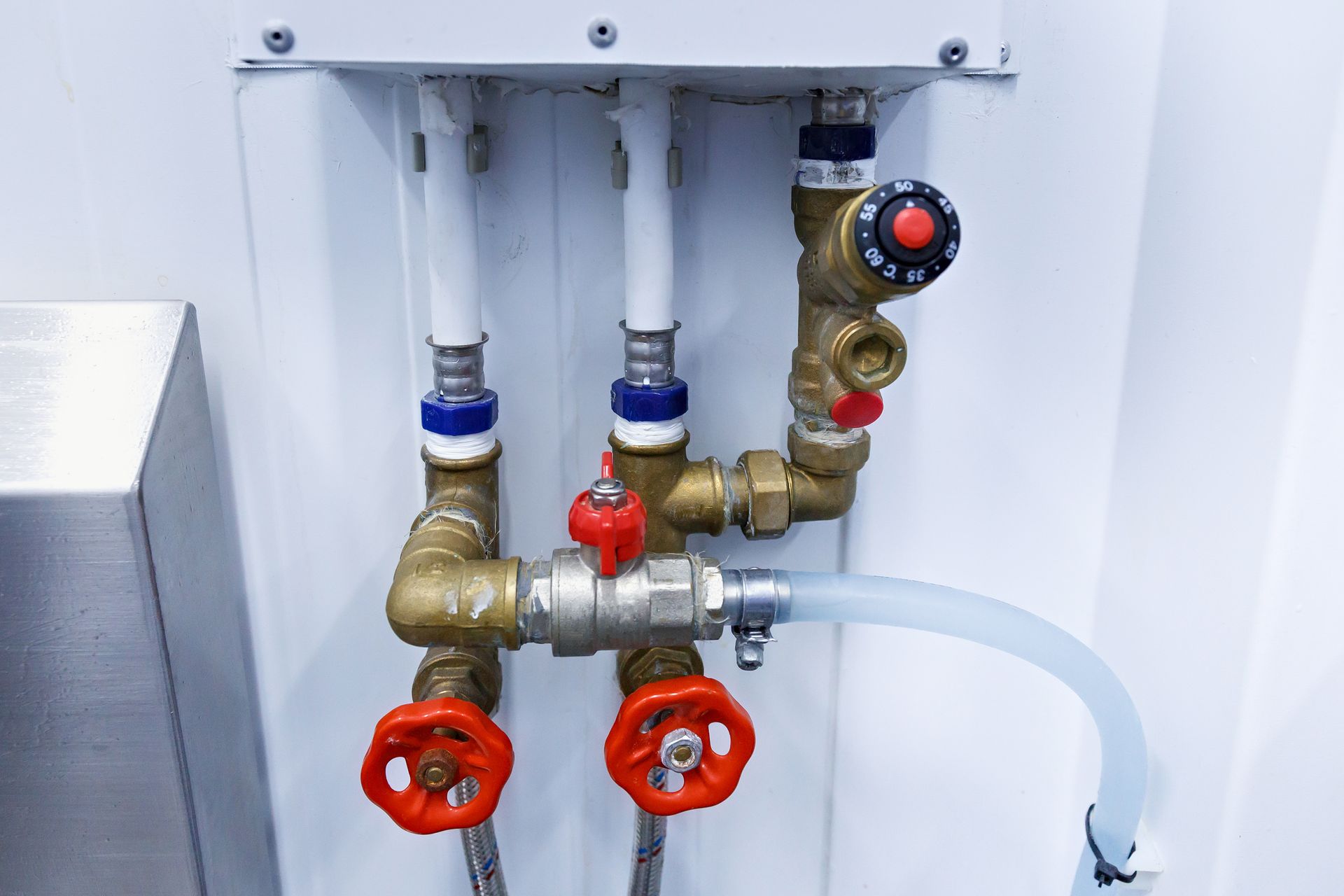 Brass pipes and valves with red handles against a white wall. Includes a temperature control knob.