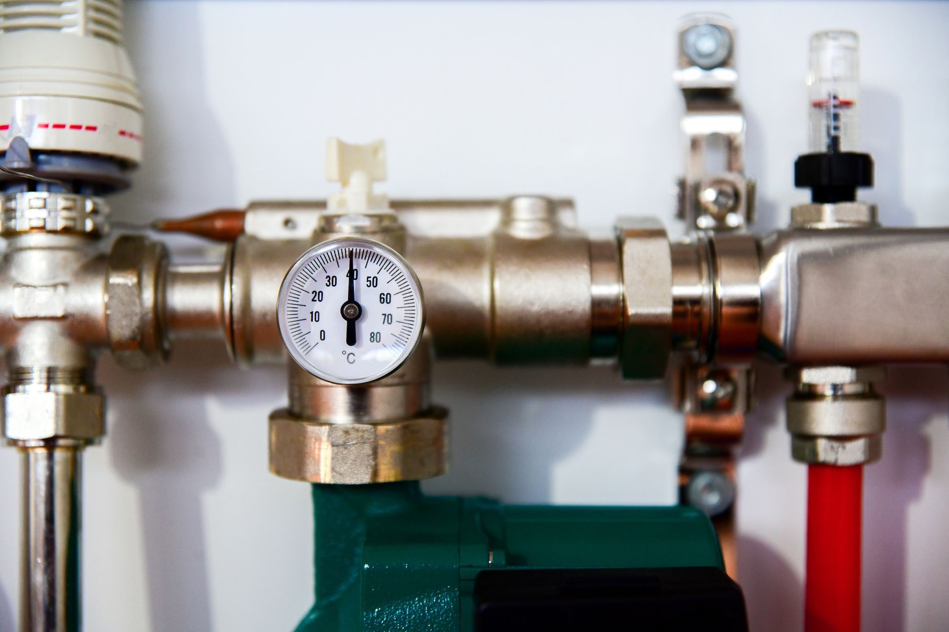 Close-up of plumbing with a pressure gauge. Metal pipes and a green pump are visible.