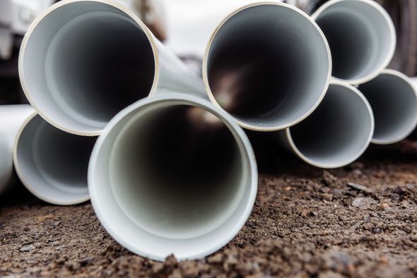 Gray PVC pipes stacked on dirt.