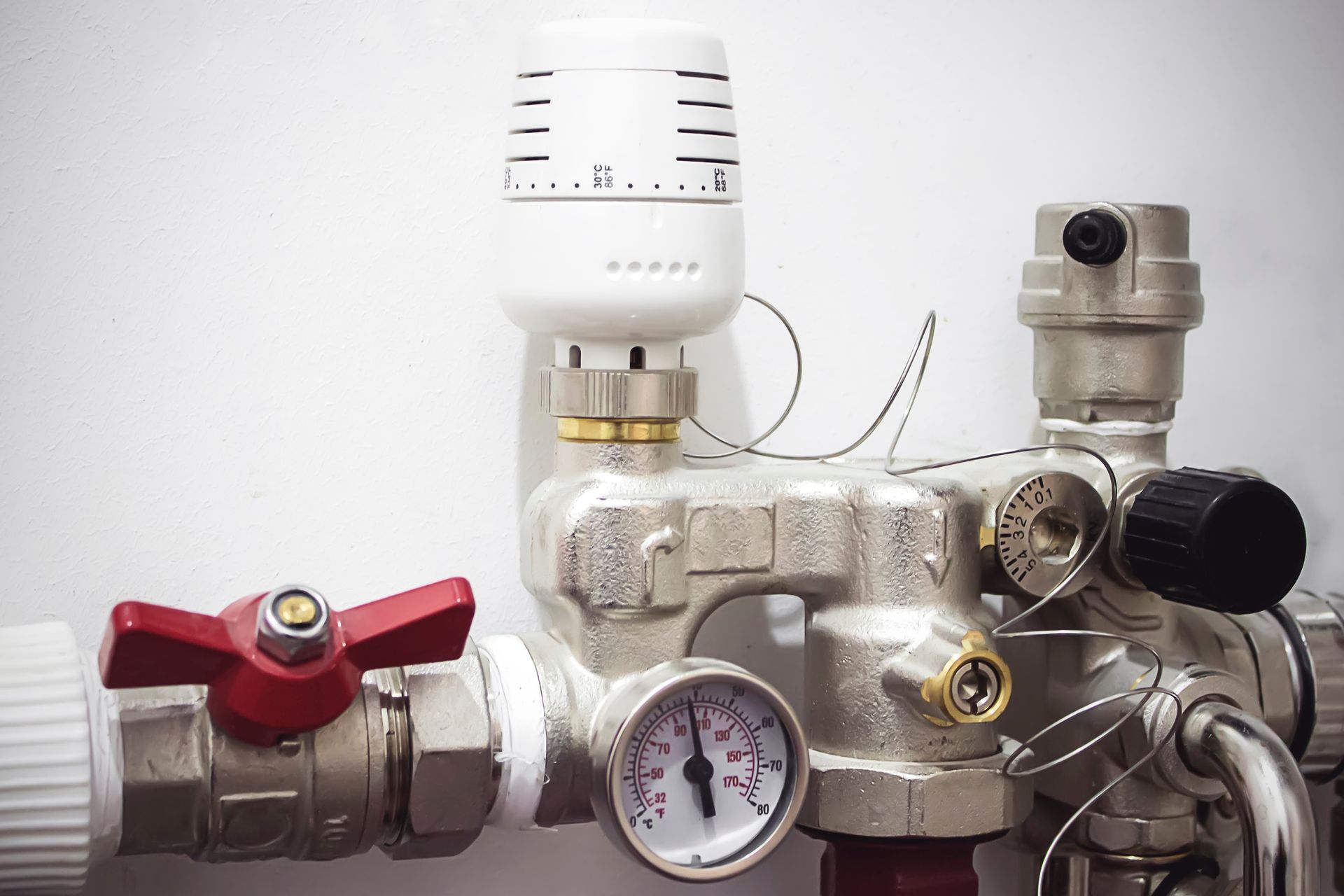 Close-up of plumbing with a red valve, pressure gauge, and thermostat.