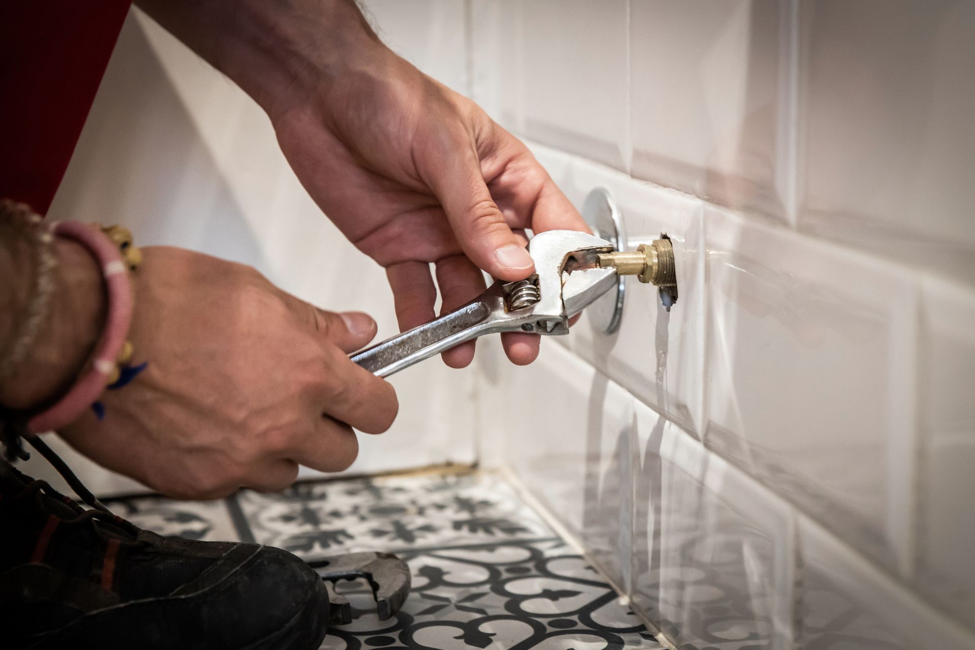 Person using a wrench to tighten a fitting in a tiled bathroom.