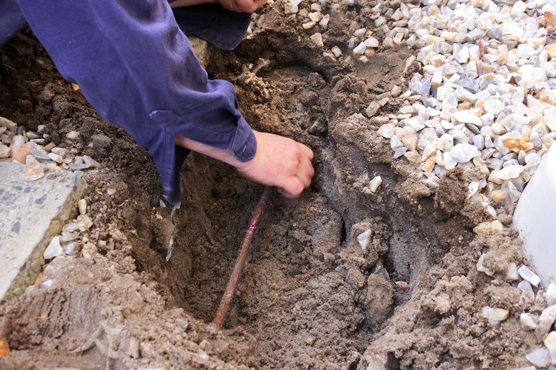 Person digging in the dirt with a tool, near pebbles.