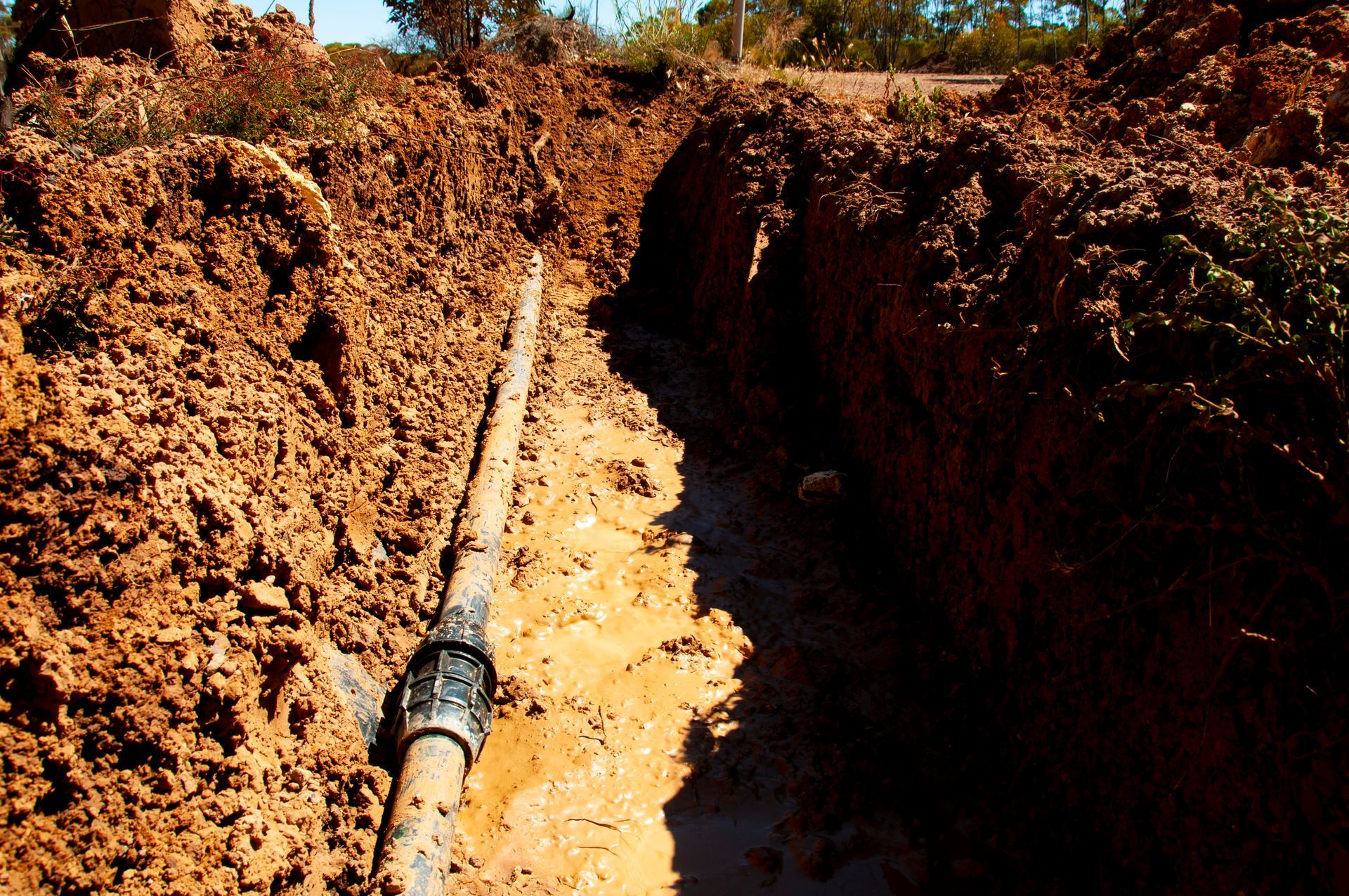 Trench dug in muddy ground, containing a pipe.