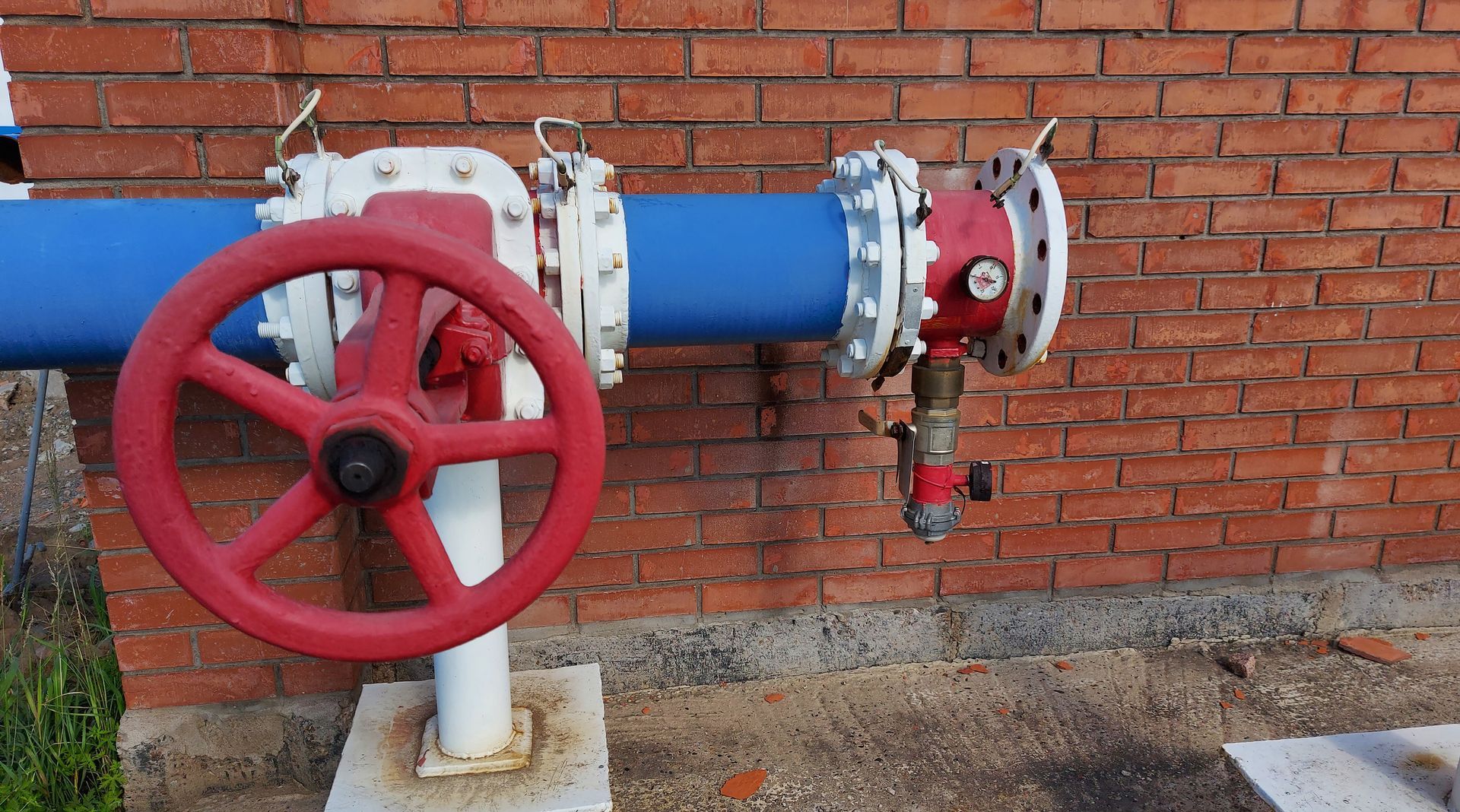 Red-handled valve on blue pipe, against a brick wall.