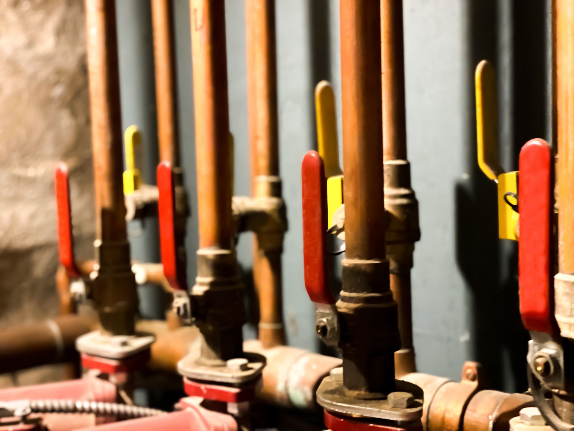 Copper pipes with red and yellow valves, possibly plumbing in a basement.