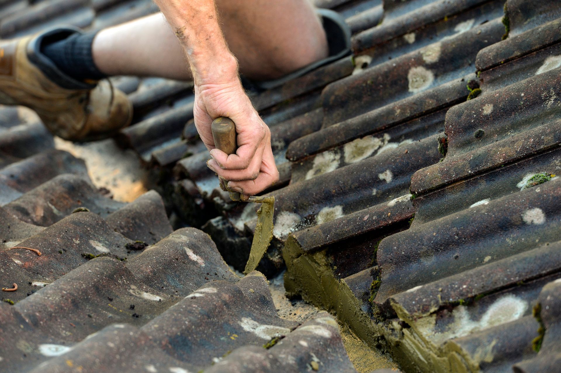 Person on a roof repairs damaged tiles with a tool.