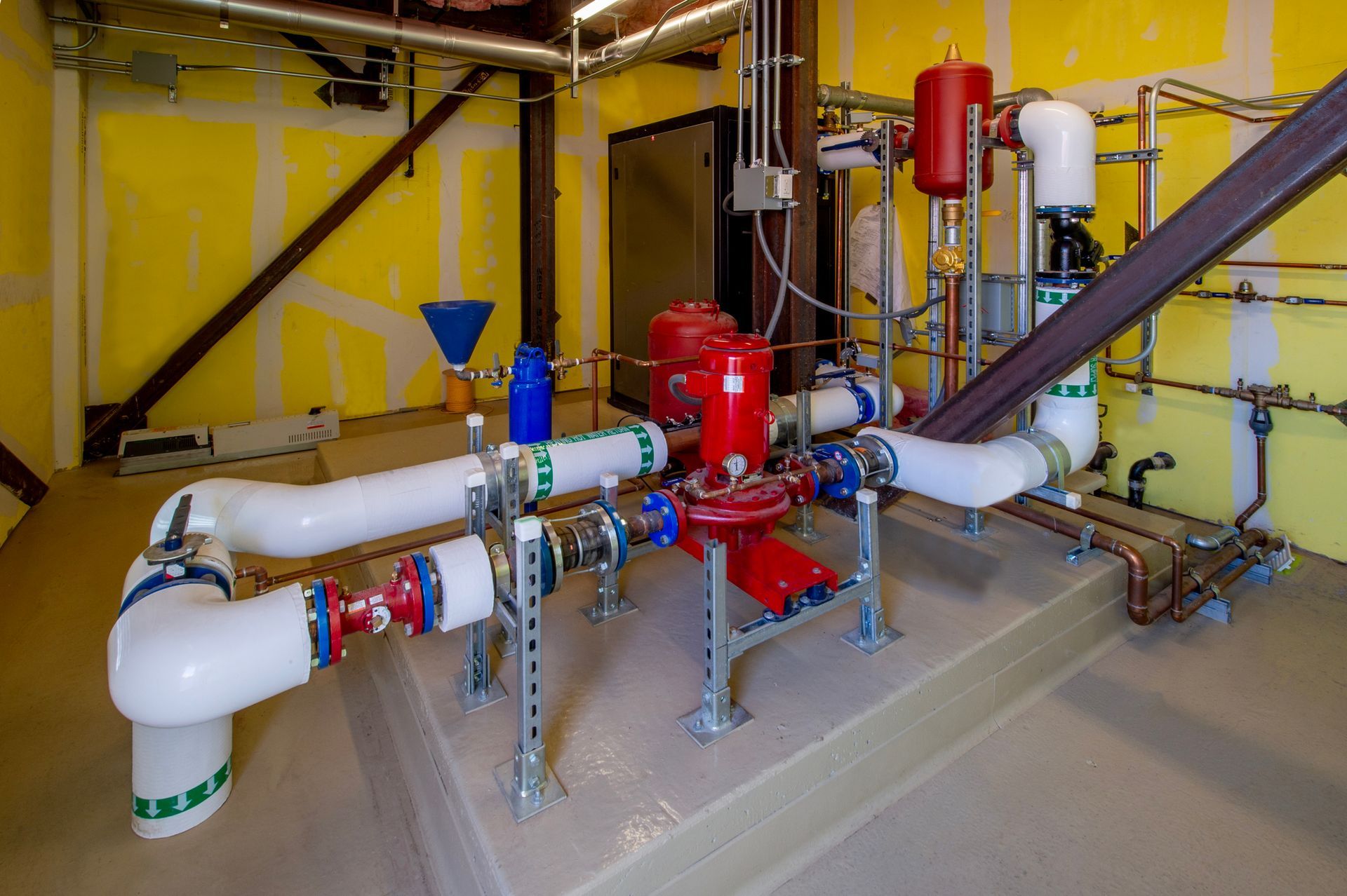 Plumbing and mechanical equipment in a utility room. White, red, and blue pipes with a red pump.