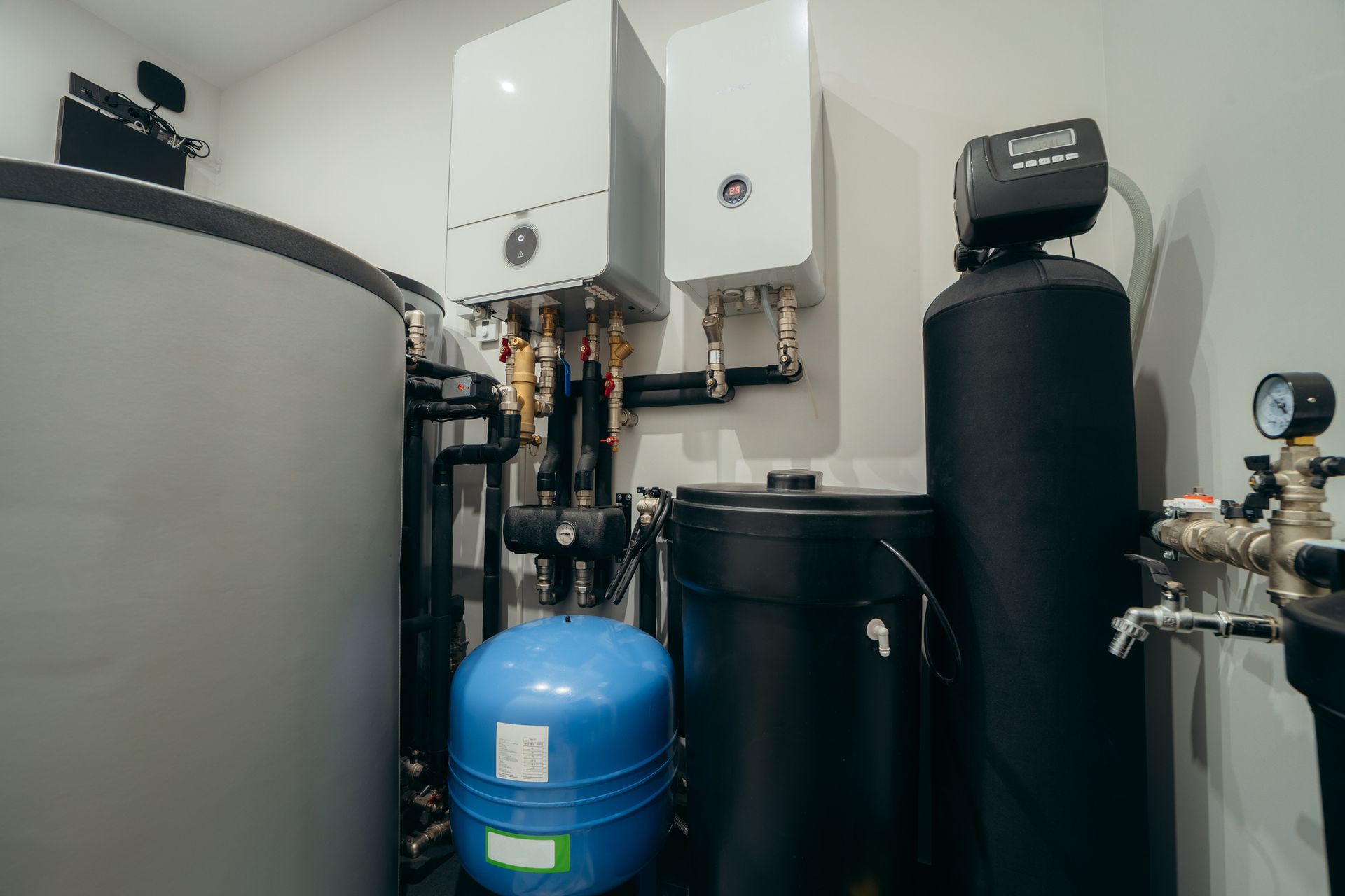 Interior view of a utility room with water tanks, pipes, and a water heater, various shapes, and sizes, mostly dark colors.