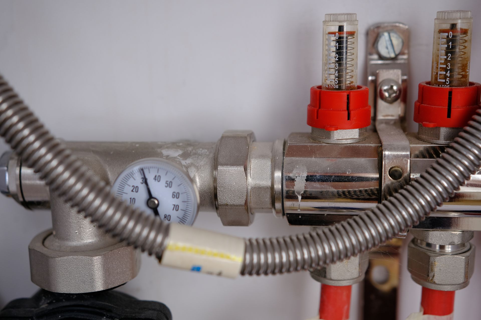 Close-up of heating system components: a pressure gauge, flow meters with red tops, and coiled metal tubing.
