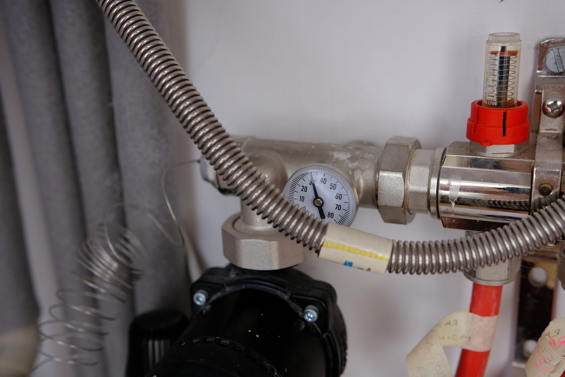 Close-up of water pipes with a gauge showing pressure and a flow meter with a red knob.
