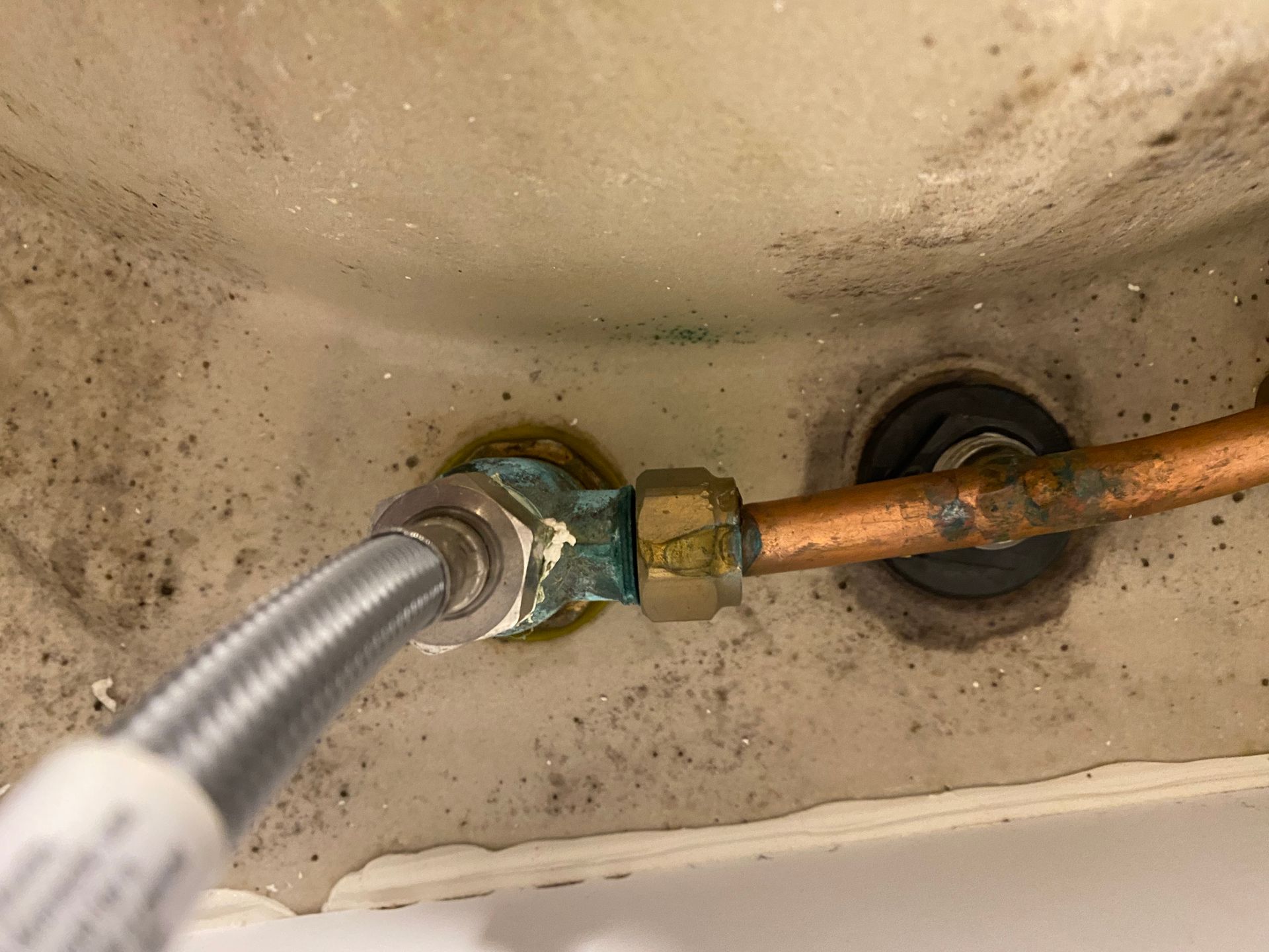Copper pipe connection with green corrosion, water supply line attached.