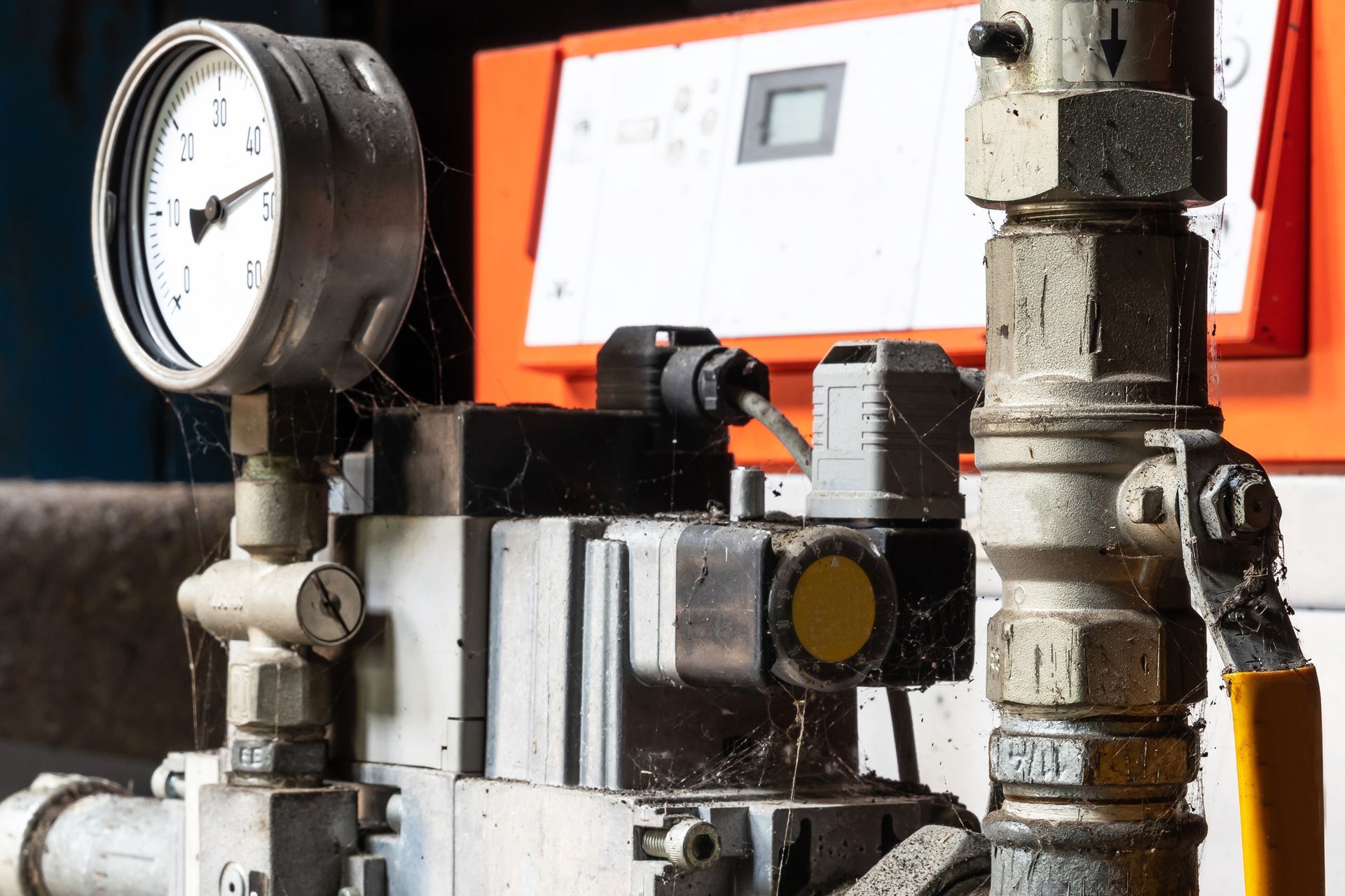 Pressure gauge and valves on industrial equipment; orange background.